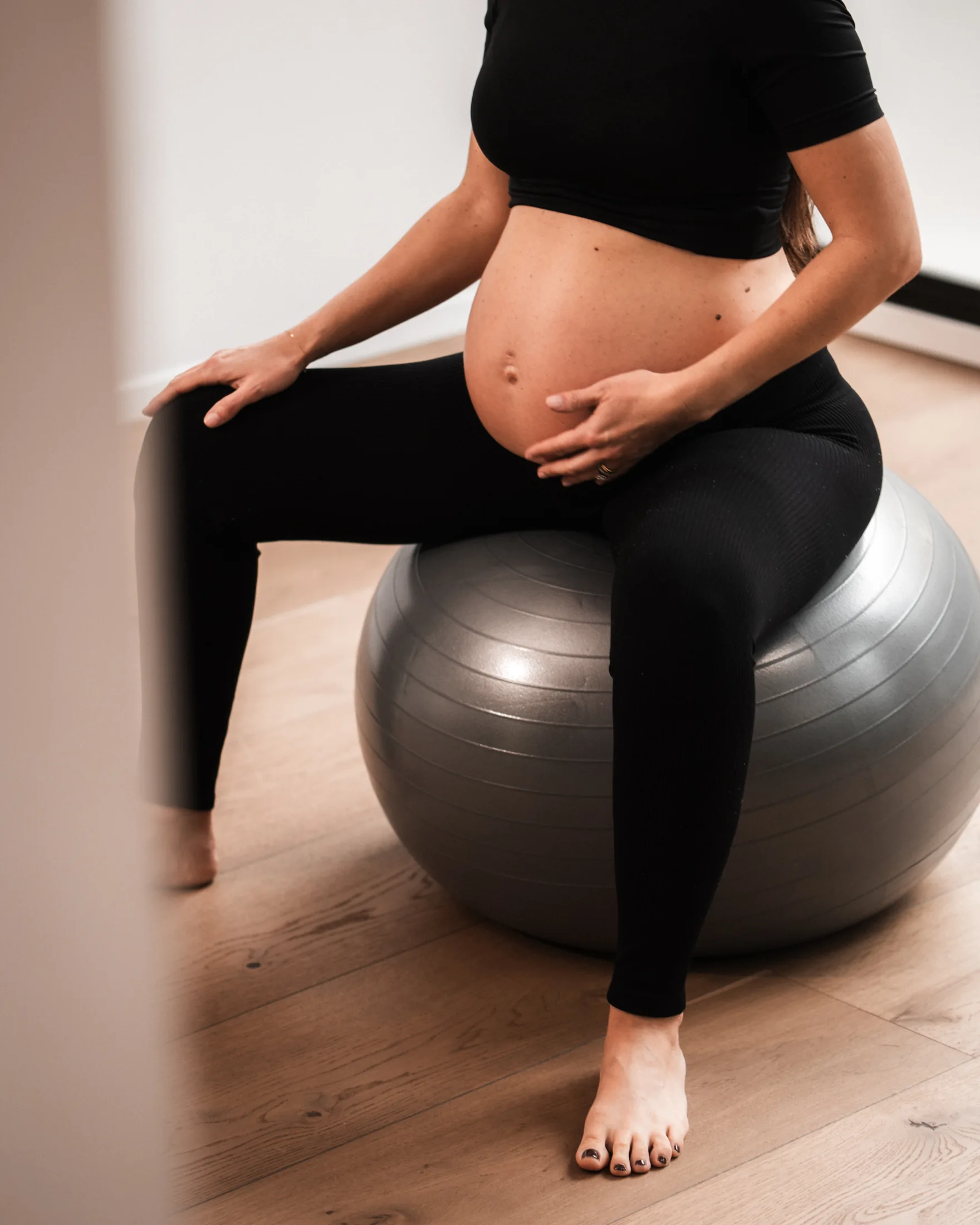 Donna in gravidanza seduta sulla fitball, mani sul ventre