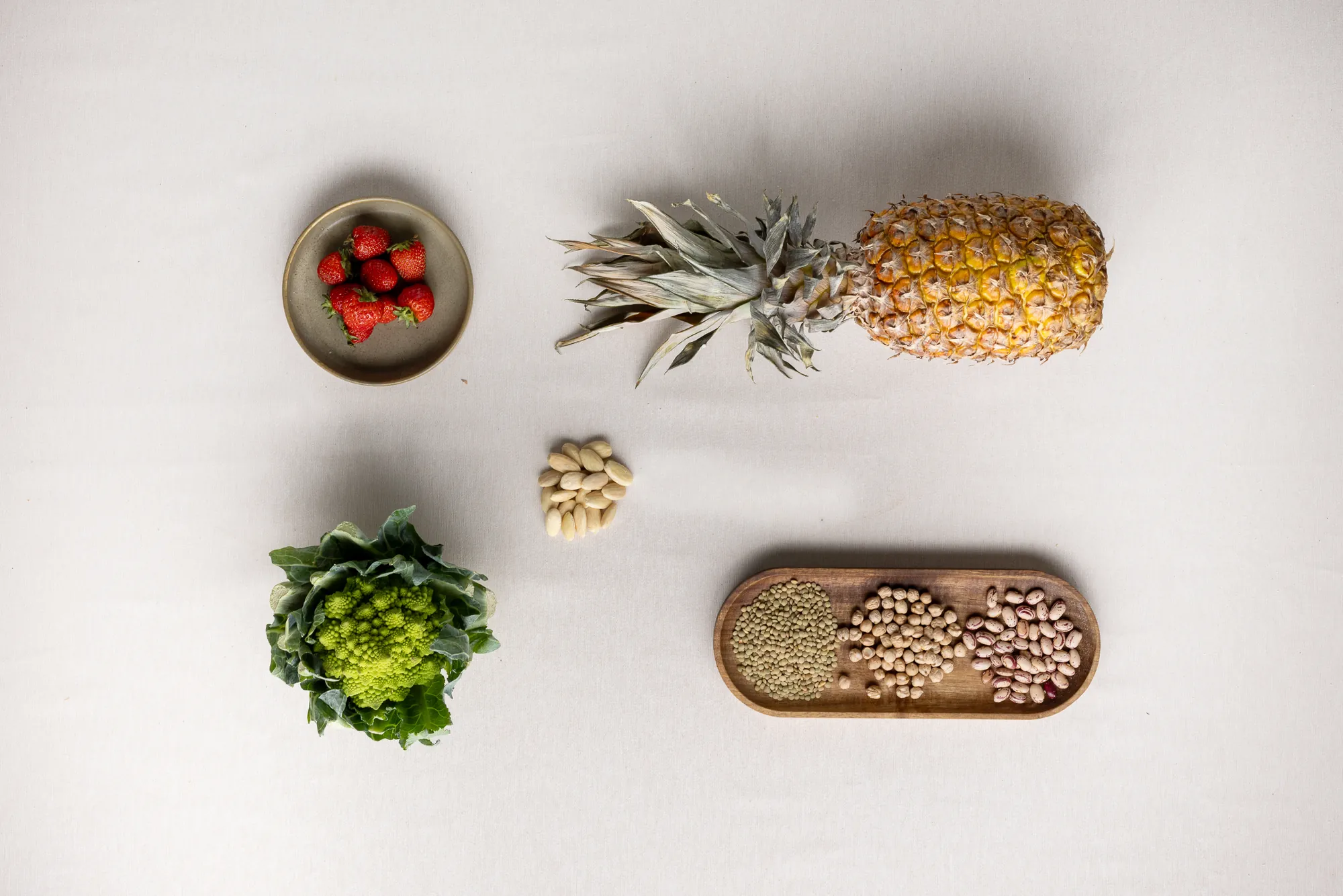 Ananas, legumi, romanesco, fragole e mandorle su fondo bianco