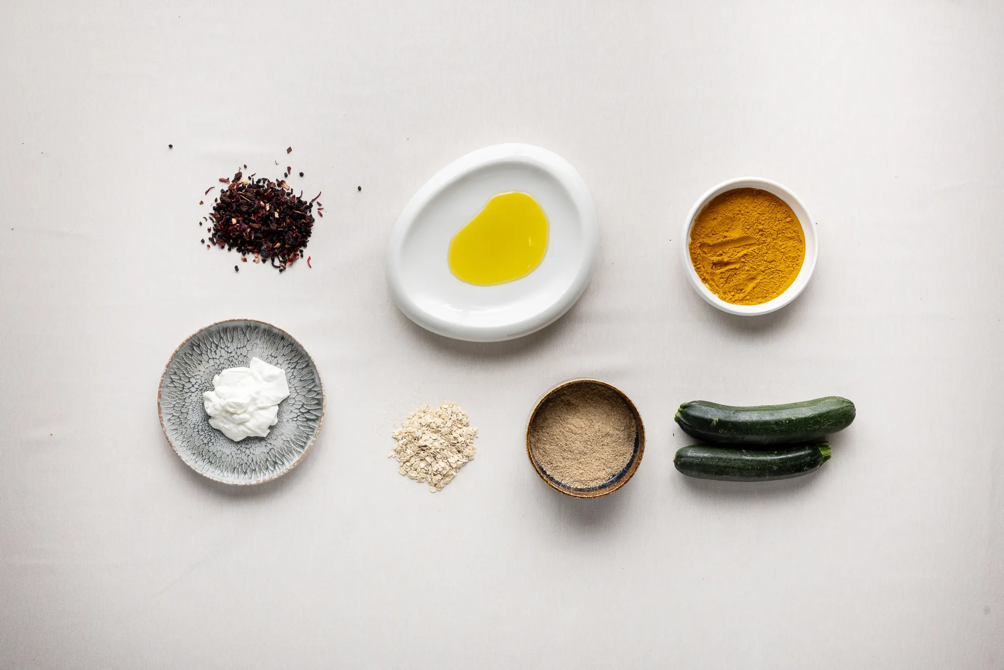 Curcuma, olio extravergine, zucchine e farina integrale su fondo bianco