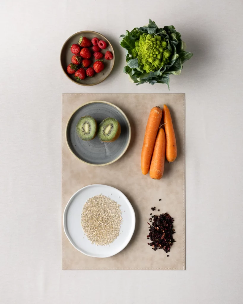Fragole, romanesco, kiwi, carote, riso e ibisco su fondo chiaro